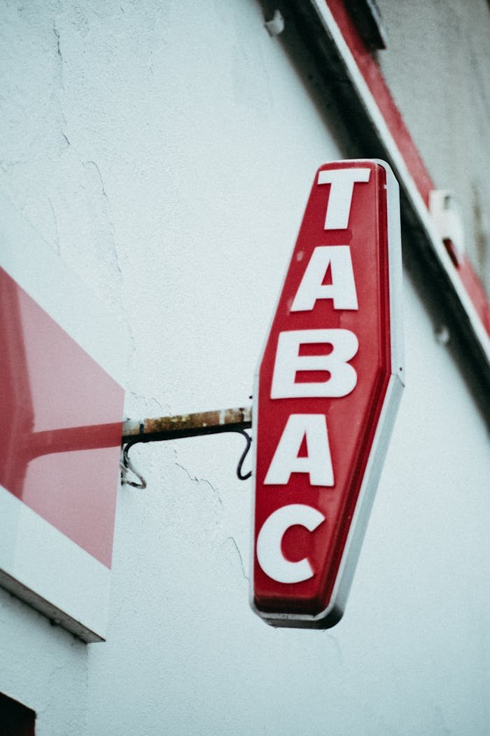 A vintage red Tabac store sign mounted on a white urban wall.