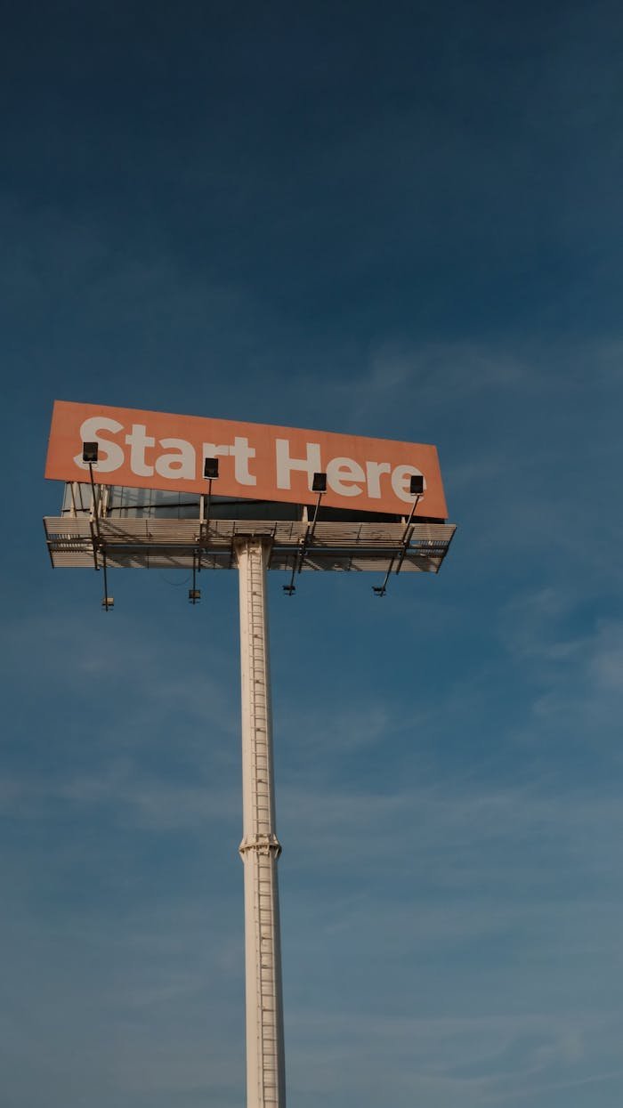 A tall billboard with 'Start Here' message set against a clear blue sky.